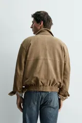 Cazadora de piel con acabado en ante, de corte relajado, con cuello solapa, cierre frontal con cremallera oculta por solapa con botones a presión, bolsillos laterales de vivo y bajo elástico.