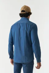 Camisa de jean azul de manga larga con dos bolsillos frontales con solapa abotonada.