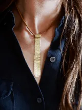 Collar de diseño minimalista con dije alargado de bronce con textura martillada, suspendido de un cordón de cuero fino.