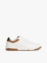 Zapatillas de corte bajo estilo retro baloncesto, confeccionadas en piel blanca con paneles de textura a contraste en color marrón y verde oliva en el talón. Presentan suela de goma dentada, cierre con cordones y logo de Tommy Hilfiger en el lateral y la lengüeta.