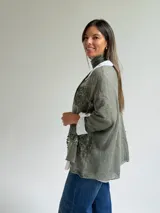 Sweater de punto color verde oliva con diseño de paneles horizontales de encaje floral, corte holgado y mangas tres cuartos. Incluye una bufanda del mismo tono y tejido, y se presenta superpuesto sobre una camisa blanca de cuello clásico.