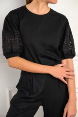 Remera negra de algodón con mangas cortas abullonadas que presentan detalles de encaje bordado y calado en los extremos.