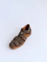 Sandalias cangrejeras de gamuza color marrón, con punta redonda, taco bajo, talonera cerrada y tira con hebilla metálica ajustable en el tobillo.