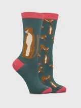 Par de medias largas de algodón, una con un diseño grande de felino sentado y la otra con un patrón repetitivo de felinos en diferentes poses. El color principal es verde azulado oscuro, con detalles en marrón y blanco para los felinos, y elástico y talón/punta en color rosado.