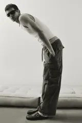 Pantalón cargo verde oliva de corte amplio, con cintura elástica ajustable con cordón, bolsillos laterales, bolsillos traseros con solapa y botón a presión, bolsillos cargo con solapa en las piernas, pliegues en la rodilla y cordón ajustable en el bajo.