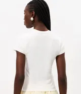 Remera baby tee de algodón color blanco, con cuello redondo, manga corta y un gran estampado frontal de una flor de lirio en tonos rosados con aplicaciones de pedrería.