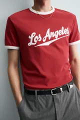 Camiseta roja de corte regular fit, con cuello redondo y mangas cortas. Presenta un estampado frontal con la frase "Los Angeles" en blanco y acabados de vivo en contraste blanco en cuello y mangas.