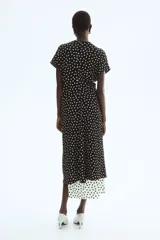 Vestido midi en punto texturizado de color negro con estampado de lunares blancos, escote redondo y manga corta. Cuenta con cintura entallada.