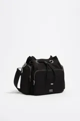 Bolso bandolera Bimba y Lola de estructura blanda en color negro, con cierre de cordón ajustable, bolsillos exteriores con cierre y asa regulable de tejido. Incluye el logo de la marca estampado en la parte frontal.
