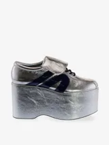 Zapatilla deportiva con plataforma extragrande, color plateado metálico con efecto arrugado en la plataforma y acabado brillante en el cuerpo. Presenta tres franjas laterales en azul marino brillante y cordones azules.