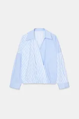 Camisa de popelín con estampado de rayas azules y blancas en diferentes direcciones, cuello solapa, escote pico cruzado, manga larga y bajo elástico.