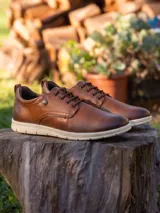 Zapatillas urbanas de cuero color marrón con cordones al tono y suela de goma blanca. Presentan un diseño de corte bajo con detalle de remache metálico en el lateral.