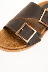 Sandalias de cuero color marrón oscuro con dos tiras anchas ajustables mediante hebillas metálicas rectangulares. Presentan plantilla anatómica de corcho y suela de goma estriada.