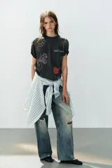 Camiseta oversize de algodón con efecto lavado, cuello redondo y manga corta. Presenta múltiples aplicaciones de brillos y strass con motivos coloridos de Smiley, incluyendo estrellas, corazones y caras sonrientes.