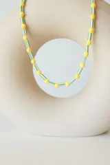 Collar tipo choker de cuentas plásticas en colores verde lima y amarillo, con diseño de cuentas cilíndricas y esféricas intercaladas. Incluye una cadena de extensión para ajustar el largo.