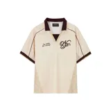 Camiseta de manga corta color beige, estilo fútbol, con cuello polo en color marrón oscuro y abertura en V. Presenta ribetes marrones en mangas y hombros, paneles laterales de malla texturizada y estampados frontales: texto "by artists for artists" y un monograma estilizado en color marrón oscuro.