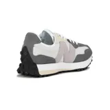 Championes urbanos New Balance modelo 327, con diseño retro inspirado en los años 70. Presentan una combinación de paneles de gamuza gris y nylon blanco, con el logo 'N' característico en el lateral y suela de goma con relieve extendido hacia el talón.