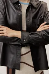 Camisa de cuero color negro, de manga larga con puños abotonados, cierre frontal con broches metálicos y un bolsillo aplicado en el pecho.