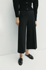 Pantalón culotte negro de tiro alto con bolsillos delanteros, pernera ancha y corta, y raya marcada al frente. Cuenta con cierre lateral con cremallera oculta.