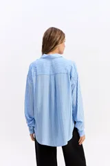 Camisa de manga larga con estampado de rayas verticales en tonos azul y blanco. Presenta cuello clásico, cierre frontal con botones y dos bolsillos tipo cargo en el pecho. Su diseño es de corte relajado y holgado.