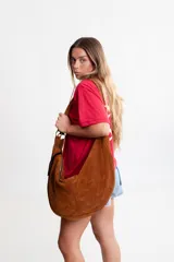 Cartera tipo hobo de gran tamaño, confeccionada en cuero descarne color rojo, con diseño artesanal y correa integrada al cuerpo de la cartera.