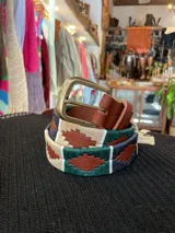 Cinturón de cuero en tono tostado con bordado a mano de hilos encerados en tonos marrones y beige con motivos geométricos, y hebilla metálica rectangular.