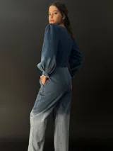 Mono largo de jean azul con lavado artesanal, escote en V regulable con cierre invisible, mangas largas abullonadas y lazo en la cintura.