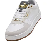 Championes Puma Court Classic de diseño urbano, confeccionados en cuero sintético blanco con refuerzos de gamuza en tono beige. Presentan detalles en azul marino en la lengüeta y el talón, junto con el logo de la marca en dorado. Cuentan con suela de goma color caramelo.