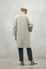 Chaqueta tipo trench color beige, de corte holgado y largo midi. Presenta cuello camisero, cierre frontal con botones a tono y mangas largas. Confeccionada en tejido repelente al agua.
