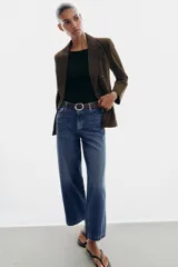 Jeans de tiro alto con pernera ancha y corte cropped. Presenta diseño de cinco bolsillos, cierre frontal con cremallera y botón, e incluye un cinturón oscuro con hebilla metálica.