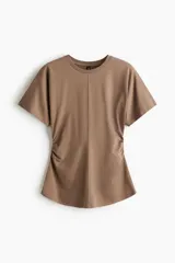 Remera color marrón de manga corta y cuello redondo, confeccionada en punto de algodón. Presenta costura central vertical y detalles de frunces laterales para un efecto drapeado.