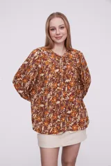 Blusa marrón con estampado de flores color naranja y blanco, con cuello redondo con abertura y mangas largas abullonadas.
