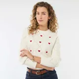 Sweater de punto color blanco con diseño de rombos en relieve y pequeños corazones rojos bordados. Presenta cuello redondo y puños acanalados.
