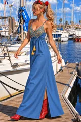 Vestido largo de denim de corte solera, color azul, con tirantes finos ajustables, escote en V y bordado dorado en el pecho. Cuenta con cordón ajustable en la cintura con borlas y tajo frontal en la falda.