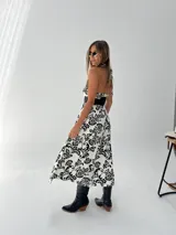 Vestido midi blanco con estampado floral negro, escote halter y cinturón ancho negro.