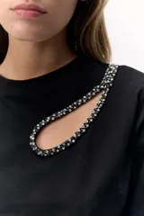 Remera negra de algodón con cuello redondo y manga corta. Presenta un calado en el hombro con detalle de pedrería.