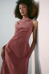 Vestido midi de piel color rosado, con cuello redondo y diseño sin mangas. Presenta costuras marcadas y cierre en la espalda con cremallera oculta.