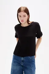 Remera negra de viscosa con textura acanalada, cuello redondo y mangas cortas terminadas en volados.