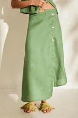 Falda midi verde de lino, con diseño asimétrico, tajito frontal y cierre lateral con botones de madera con ojales bordados.