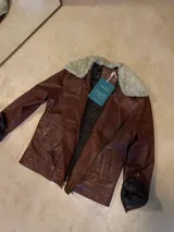 Campera de cuero ovino marrón, de corte biker, con cuello de corderito desmontable y cierre frontal cruzado.