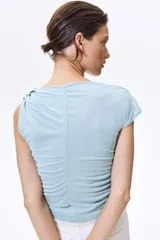 Top de punto celeste con leve brillo, sin mangas, con escote drapeado y detalle metálico martillado en un hombro. Presenta costuras fruncidas en los laterales para realzar el efecto drapeado.