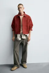 Cazadora de algodón color terracota, de corte cropped y calce holgado. Presenta cuello solapa, manga larga con puño abotonado, dos bolsillos de vivo en el pecho y bolsillos laterales en la cadera. Cierre frontal con botonadura oculta.