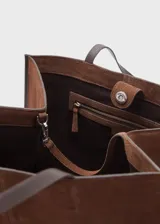 Bolso tipo shopper de piel de serraje en color marrón, con diseño de paneles y doble asa de hombro. Cuenta con cierre de botón magnético y bolsillo interior con cremallera.