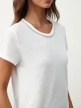 Remera negra de corte clásico con cuello redondo ribeteado con pequeñas perlas blancas.