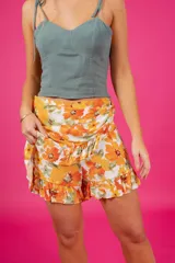 Short con diseño de pollera, tiro medio, estampado floral en tonos violeta, azul y rosado. Presenta detalle de aro de madera en la cintura, cierre lateral oculto y volados en la parte inferior.