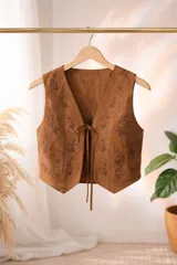 Chaleco de gamuza color marrón con bordados florales en tono oscuro y cierre frontal mediante lazos.