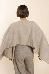 Poncho color beige con diseño a cuadros, cuello bote y terminaciones desflecadas. Tiene aberturas para los brazos en los laterales y detalles en cuero.