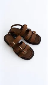 Sandalias de cuero negro con punta semicuadrada, taco cuadrado bajo y tres tiras frontales con hebillas metálicas plateadas. Cuentan con tira trasera con cierre ajustable.