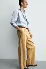 Pantalón chino straight fit de corte recto y holgado, color tostado, con pliegues frontales en la cintura, bolsillos laterales y cierre con cremallera y botón.