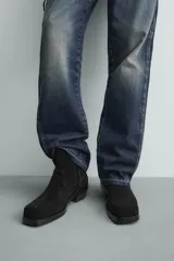 Bota estilo cowboy de caña media, confeccionada en piel con acabado de serraje. Presenta horma cuadrada, cierre lateral mediante cremallera y suela con tacón bajo.
